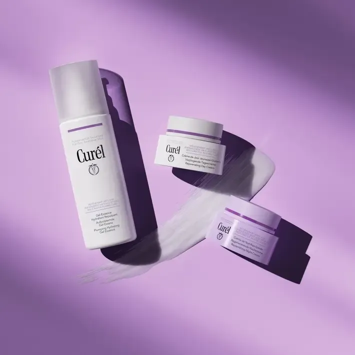 Curél anti-age Gel Essence, Rejuvenating Day Cream and Regenerative Night Cream in white and purple packaging on a purple surface with a cream swatch.