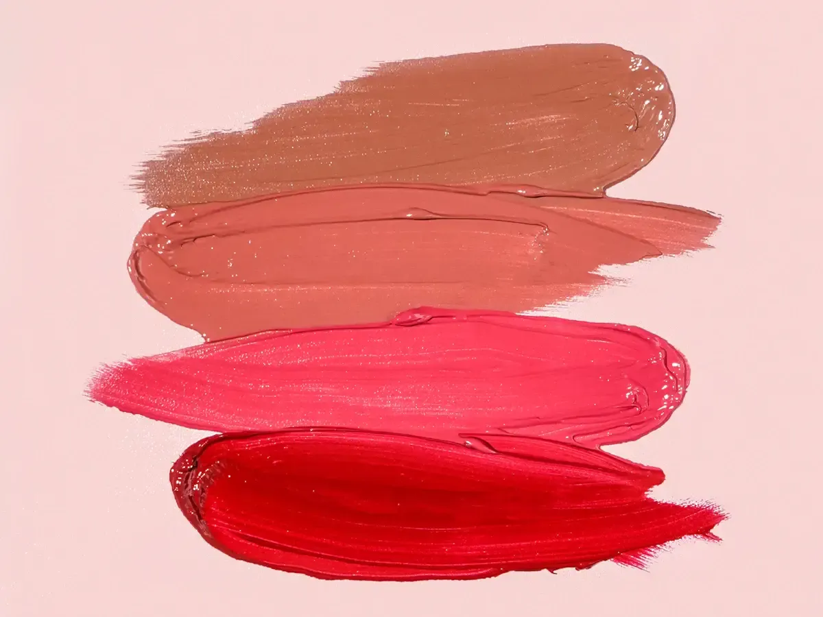 Four swatches of lipstick in brown, peach, pink, and red on a pale pink background, an illustrative stock image rather than MAC products