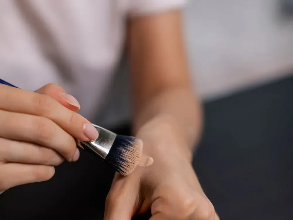 A makeup brush blending foundation on the back of a hand; stock photography, not a demonstration of Westman Atelier’s formula.